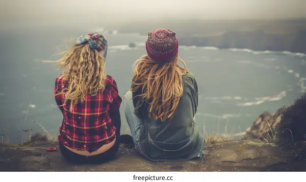 Two Women Sitting on a Cliff Overlooking the Ocean