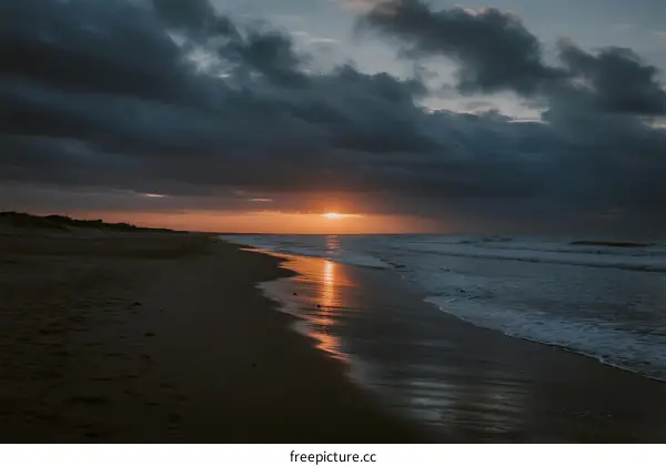 Sunset over the calm beach with dark clouds in the sky