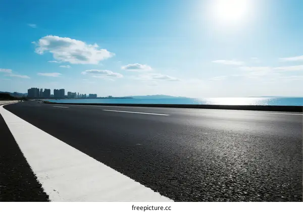 A smooth asphalt road with a clear blue sky and sea in the distance