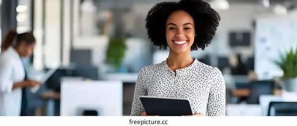 Smiling Black Woman Holding Tablet In Modern Office