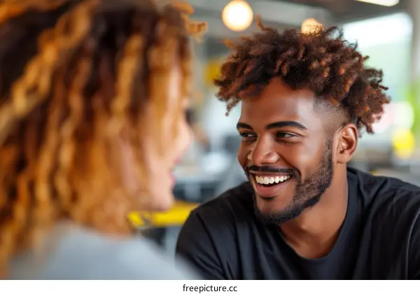 A young man with curly hair is smiling at a woman