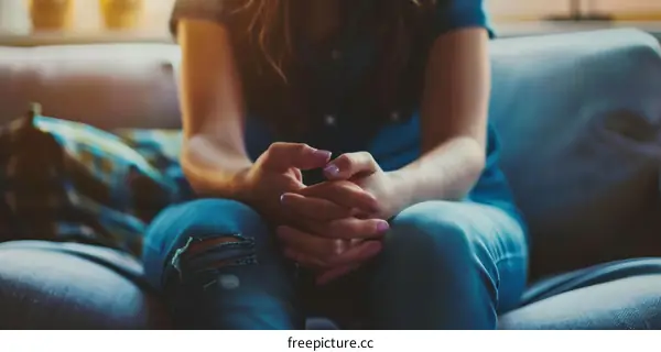A young woman sits on a couch with her hands clasped in her lap