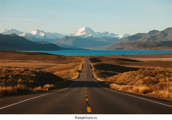 Long straight road leading to distant mountain range with blue lake