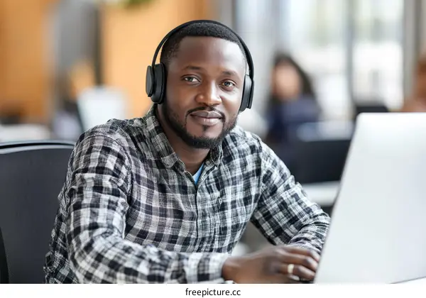African Man in Office Using Headphones and Laptop