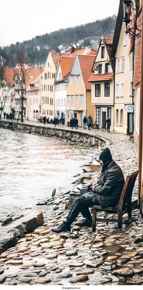 Man Sitting on a Bench by the River in a European Town