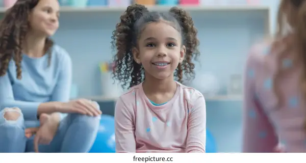 A young girl with curly hair smiling in a classroom with two other people in the background