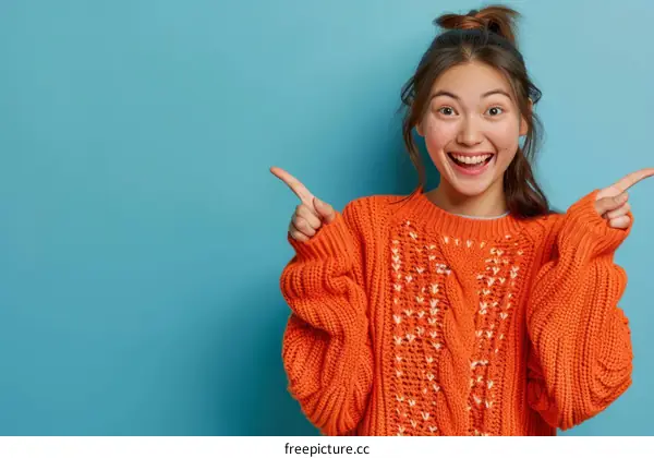 Cheerful Asian woman in orange sweater pointing fingers aside