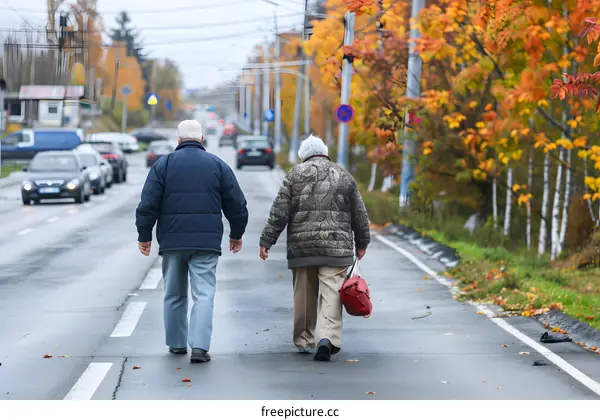 Two Elderly People Walking Down A Street In The Autumn
