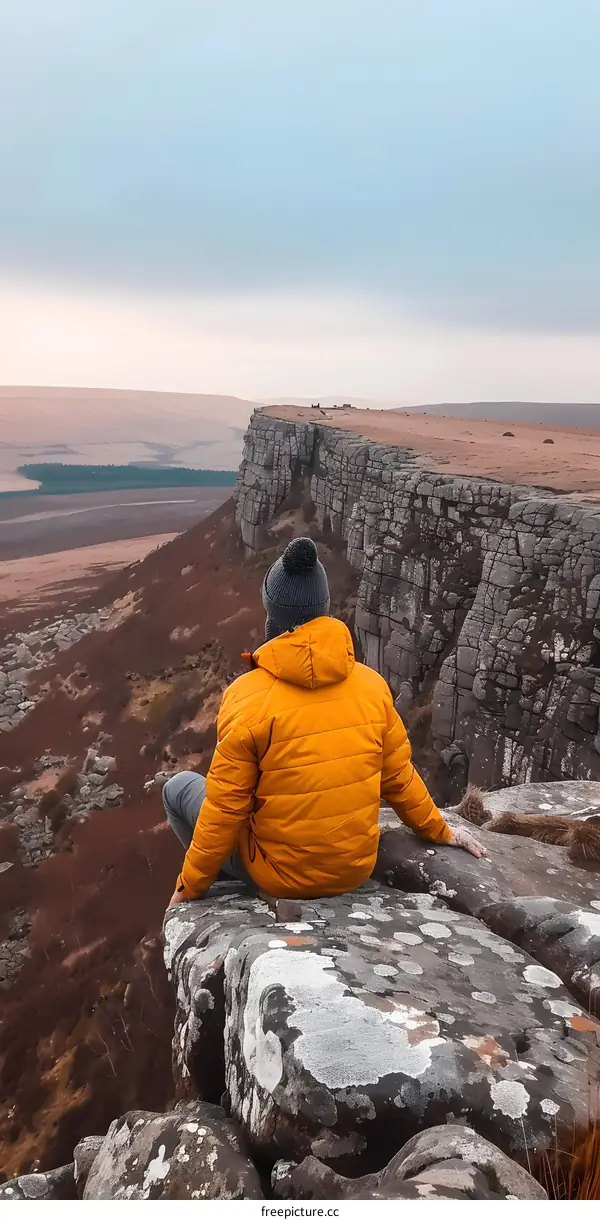 Man Sitting on a Cliff Edge Looking at a Mountain Range