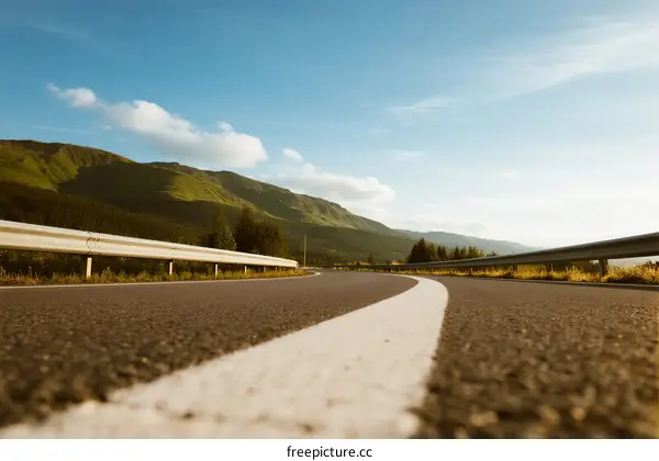 A scenic road with white lines leading to green mountains under a clear sky