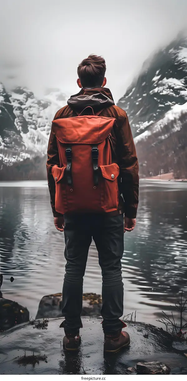 Man with Backpack Standing on a Rock by a Lake in the Mountains