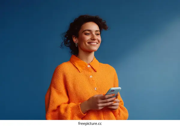Smiling Woman Holding Phone in Orange Sweater Against Blue Background