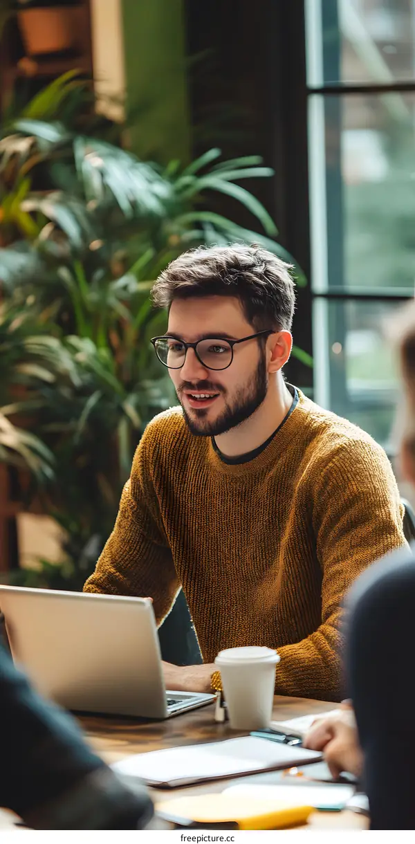 Man in a Yellow Sweater Talking on Laptop with Coffee in Hand
