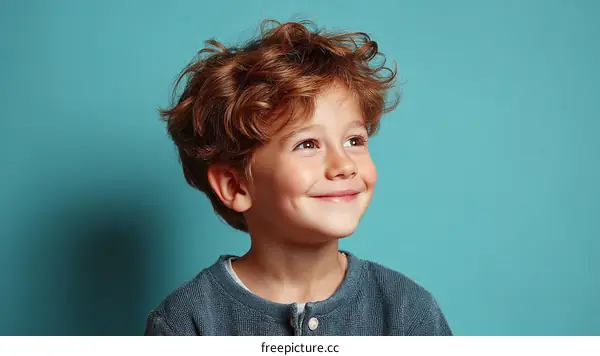 A Young Boy with Curly Red Hair Smiling Against Blue Background