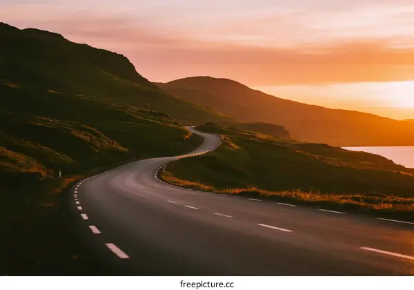 Winding road at sunset with green hills and sea view