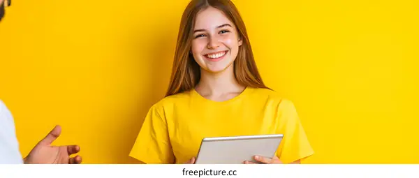 Smiling Woman Holding a Tablet Computer in Front of a Yellow Background
