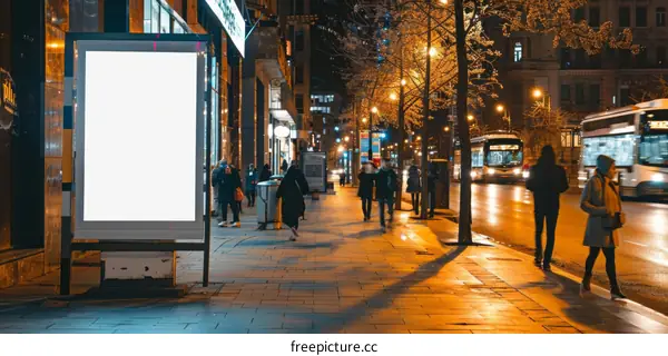 People walking on a city street at night past a blank billboard