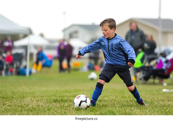 Young Boy Playing Soccer On Grass Field