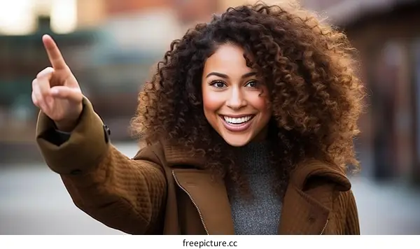 Portrait of a young woman with curly hair smiling and pointing