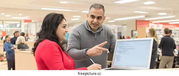 Two People Discuss Programming Code on a Laptop