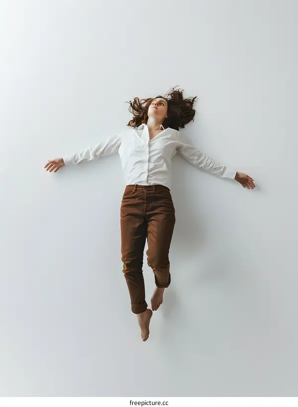 woman in brown pants and white shirt laying on her back with arms outstretched