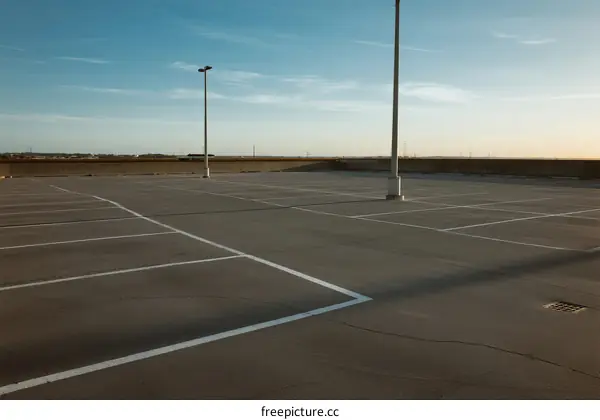 Empty parking lot under clear sky with white lines and light poles