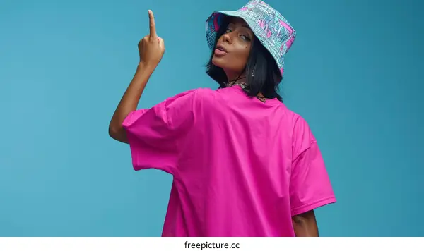 A woman of African descent wearing a pink shirt and a bucket hat points her middle finger