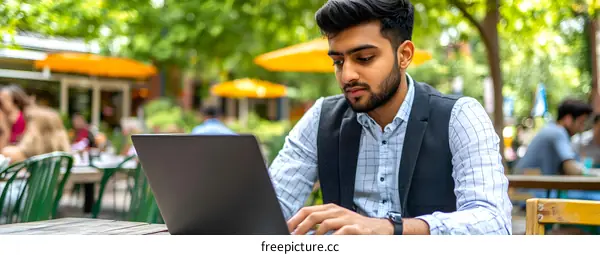 Young Indian Man Working on Laptop at Outdoor Cafe