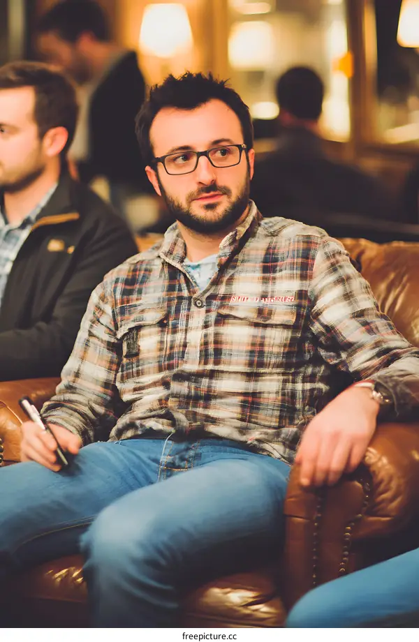 Man Sitting On Leather Couch In Plaid Shirt