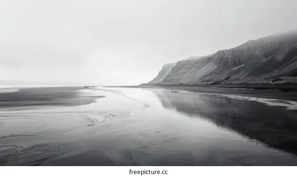 Black and white beach photograph with a towering cliff in the distance