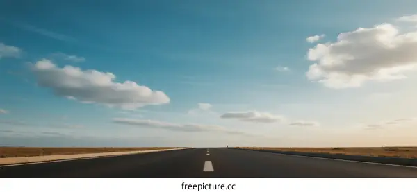 Open road under a clear blue sky with scattered clouds