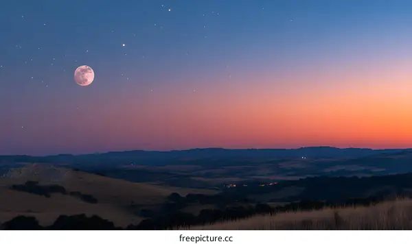 Full Moon Over a Hilly Landscape at Sunset