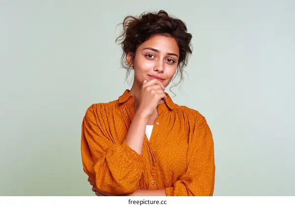 Thoughtful young woman with hand under chin in casual orange shirt