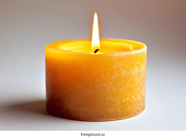 A single candle is lit on a white table against a pale yellow background.