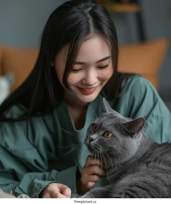 A young woman is smiling at a gray cat