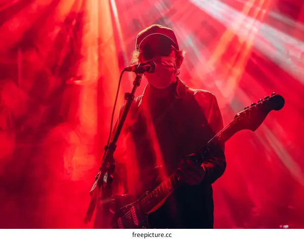 A masked musician performing on a stage with a red spotlight