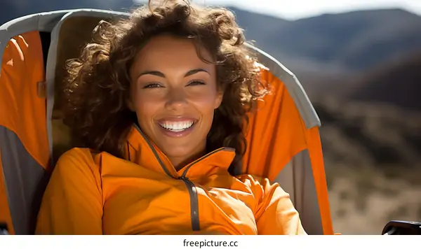 Smiling woman in orange jacket sitting in camping chair