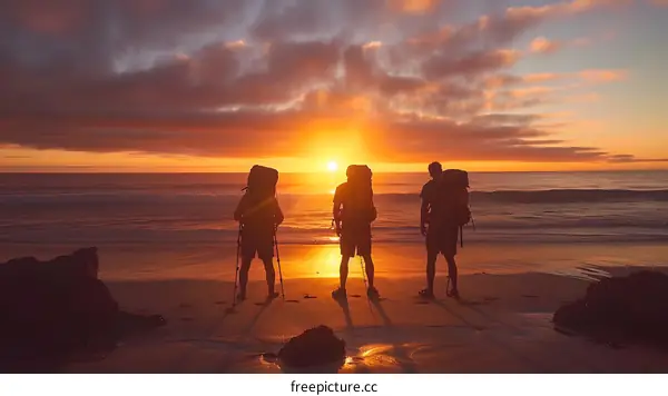 Silhouettes of Three Hikers Standing on Beach Watching Sunset