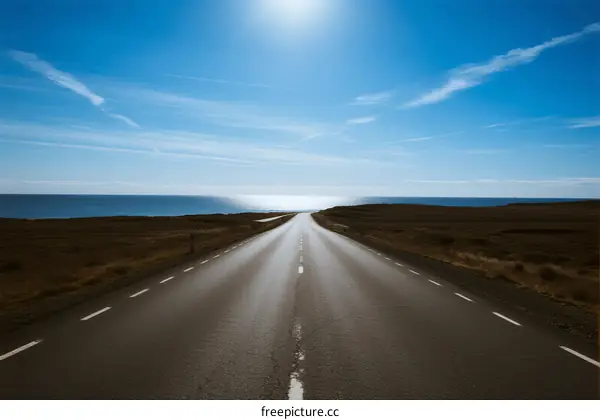 A long road stretching under a bright sun towards the sea
