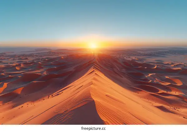 A vast expanse of sand dunes in the middle of a desert with the sun rising in the background