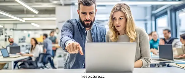 Two Coworkers Looking at a Laptop Together in an Office Setting