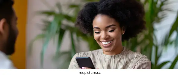 Smiling African American Woman Uses Smartphone While Chatting With Another Person