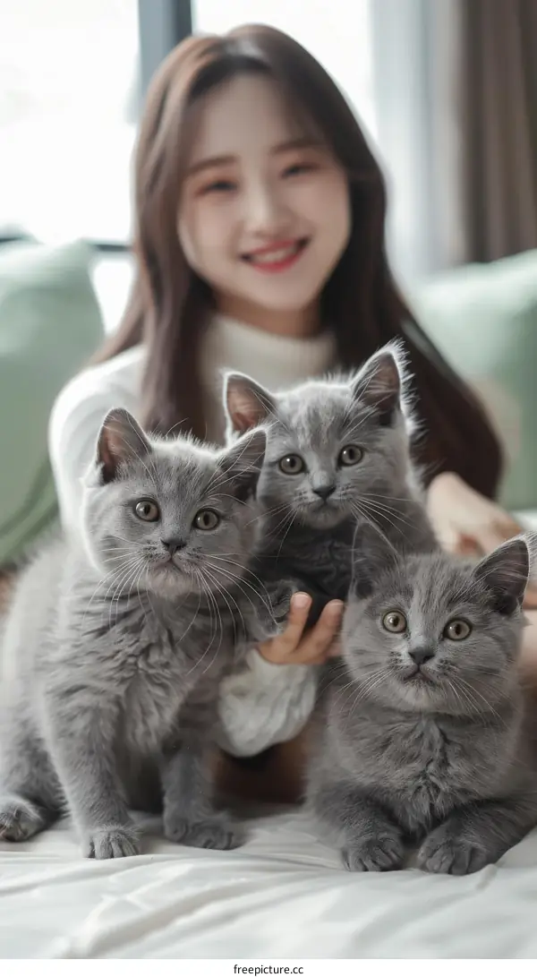 A young woman is sitting on a bed with three gray kittens.