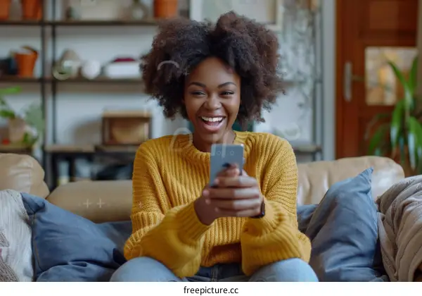 Laughing African American woman using smartphone sitting on couch at home