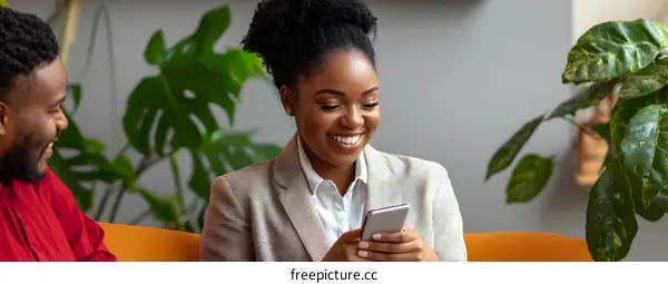 Happy Black Woman Looking at Phone While Sitting on Orange Sofa