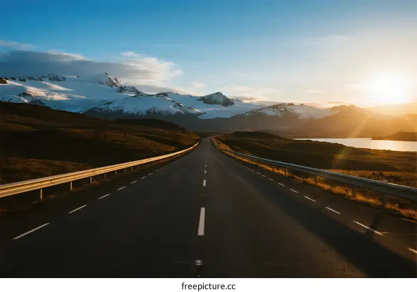 Scenic road with snow-capped mountains under a clear sky at sunset