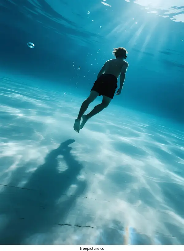 A man swimming underwater with sunlight streaming through water surface
