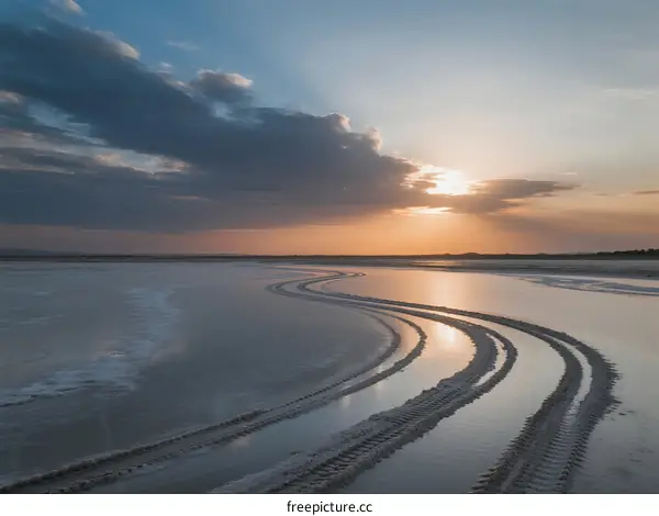 Sunset over a serene coastal area with tire tracks on the sand