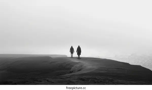 Two people walking on a hilltop overlooking the ocean