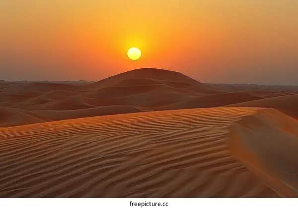 A vast desert landscape with a large sand dune in the foreground and a setting sun in the background